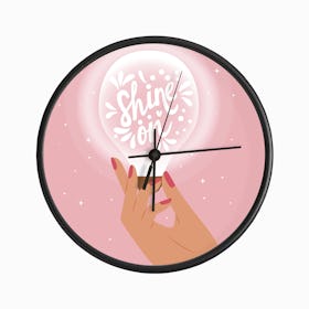 Shine On Hand Lettering With Hand Holding A Light Bulb On Pink Clock