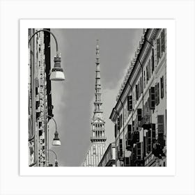 Urban View of a Historic Spire. The image depicts a black-and-white urban scene featuring a tall, ornate spire rising prominently in the center. The spire is framed by two rows of buildings with numerous windows and balconies, creating a symmetrical perspective. Street lamps hang from curved poles on the left side of the image, adding to the urban atmosphere. The architectural details and the height of the spire make it a focal point, suggesting it is a significant landmark. Art Print