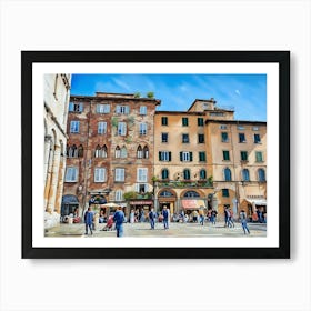 Piazza dell'Anfiteatro in Lucca. The vibrant Piazza dell'Anfiteatro in Lucca, Italy, is a unique elliptical square built on the remains of an ancient Roman amphitheater. Surrounded by colorful historic buildings, the square is bustling with life, featuring outdoor cafes, shops, and visitors enjoying the lively atmosphere. 2 Art Print