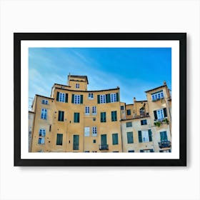 Piazza dell'Anfiteatro in Lucca. The vibrant Piazza dell'Anfiteatro in Lucca, Italy, is a unique elliptical square built on the remains of an ancient Roman amphitheater. Surrounded by colorful historic buildings, the square is bustling with life, featuring outdoor cafes, shops, and visitors enjoying the lively atmosphere. Art Print