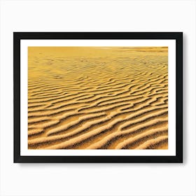 Sand Dune Texture. The image showcases a close-up view of a sandy surface, featuring a mesmerizing pattern of undulating waves and ridges. The sand is a warm, golden yellow, with darker lines and shadows accentuating the intricate texture. The light catches the peaks of the dunes, creating a subtle shimmer. The overall mood is serene and tranquil, evoking a sense of vastness and natural beauty. Art Print