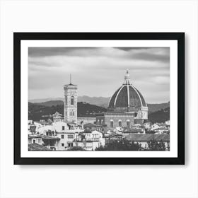 Florence Cathedral and Giotto's Campanile. This black and white photograph captures the iconic Florence Cathedral (Duomo) and Giotto's Campanile in Florence, Italy. The image showcases the architectural grandeur of the cathedral's large dome and the intricate details of the bell tower, set against a backdrop of rolling hills and a cloudy sky. The foreground includes a mix of traditional Italian buildings, adding to the historical ambiance of the scene. Art Print