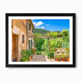 Mediterranean Spain. In the enchanting old village of Valldemossa on the idyllic Spanish island of Majorca, a picturesque scene awaits visitors. Traditional flower pots decorate the walls of the narrow streets and residential buildings, bringing color and beauty to the village's charming architecture. Art Print