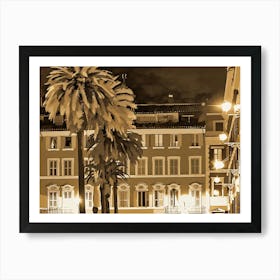 Nighttime scene with two palm trees in the foreground, their fronds silhouetted against a backdrop of a city street. The buildings are rendered in a sepia tone, with warm yellow lights emanating from windows and street lamps. The scene is bathed in a soft, warm glow, creating a sense of tranquility and charm. Art Print