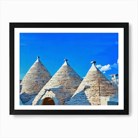 Trulli Houses in Italy. The image showcases three traditional Trulli houses, characterized by their distinctive conical roofs made of dry-stacked limestone. The houses are painted in a warm white, contrasting beautifully against the bright blue sky. The roofs are adorned with simple, white-painted finials, adding a touch of elegance. The scene is bathed in warm sunlight, casting soft shadows on the stone walls. Art Print