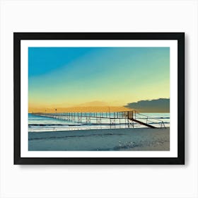 Pier at Sunset in Riviera. A long wooden pier extends out into the calm ocean waters, reaching towards a distant horizon. The sky is a vibrant blend of blue and orange, creating a picturesque sunset backdrop. The pier is constructed with wooden planks and metal railings, leading to a small platform at the end. The sandy beach stretches out in the foreground, with gentle waves lapping at the shore. Art Print