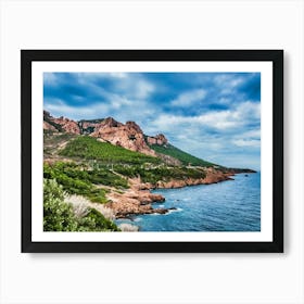 Coastal Cliffs and Blue Sea in Esterel France. The image captures a breathtaking coastal landscape with a dramatic interplay of land and sea. Rugged, reddish-brown cliffs rise from the shore, covered in lush green vegetation. The cliffs are punctuated by rocky outcroppings and a winding road that snakes along the hillside. Art Print