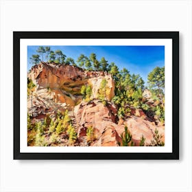 Ochres Land Majestic Cliffside Forest. This image showcases a stunning cliffside landscape adorned with lush green trees. The rocky formations exhibit a range of warm hues, from sandy yellows to deep reds, creating a striking contrast against the vibrant blue sky. The scene captures the beauty of nature's rugged terrain and the resilience of trees growing on steep, rocky surfaces. 2 Art Print