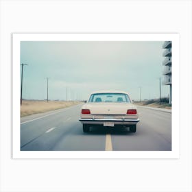 A Beige Vintage Car Drives Down A Street, With A Modern Apartment Building In The Background Art Print