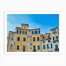 Piazza dell'Anfiteatro in Lucca. The vibrant Piazza dell'Anfiteatro in Lucca, Italy, is a unique elliptical square built on the remains of an ancient Roman amphitheater. Surrounded by colorful historic buildings, the square is bustling with life, featuring outdoor cafes, shops, and visitors enjoying the lively atmosphere. Art Print