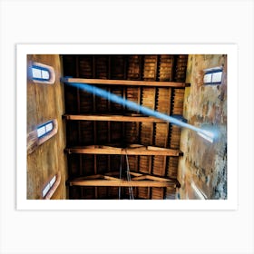 Heavenly Light. A captivating view of a wooden church ceiling in Pisa, with natural light streaming through small arched windows. The interplay of light and shadows highlights the intricate beams and aged walls, creating a serene and spiritual atmosphere. Art Print