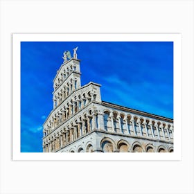 Lucca Majestic Facade: The Elegance of Romanesque Architecture. This image highlights the intricate facade of a Romanesque-style church under a vibrant blue sky. The series of arches, columns, and detailed sculptures create a harmonious display of historical craftsmanship, crowned by statues of angels that enhance the monument's grandeur. Art Print