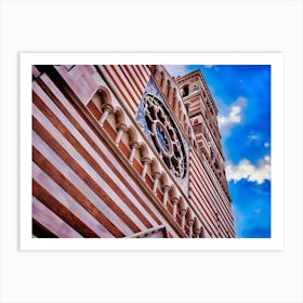 Rome: Striped Cathedral Facade with Rose Window. The image showcases the facade of a cathedral with distinctive horizontal red and white stripes. The architectural design features a series of arches supported by columns and a prominent rose window with intricate detailing. The sky in the background is a vibrant blue with scattered clouds, enhancing the visual appeal of the structure. Art Print