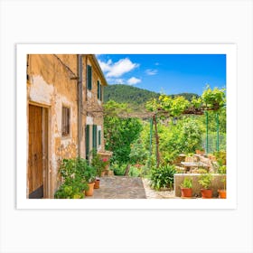 Mediterranean Spain. In the enchanting old village of Valldemossa on the idyllic Spanish island of Majorca, a picturesque scene awaits visitors. Traditional flower pots decorate the walls of the narrow streets and residential buildings, bringing color and beauty to the village's charming architecture. Art Print