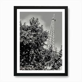 Eiffel Tower Behind Foliage. The image depicts the iconic Eiffel Tower partially obscured by dense foliage. The tower's intricate iron lattice structure rises prominently against a cloudy sky, creating a striking contrast with the dark leaves in the foreground. This juxtaposition of nature and architecture highlights the blend of urban and natural elements in Paris. Art Print