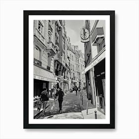 Paris Strolling Through a European Alley. The image depicts a charming European alleyway with cobblestone streets and classic architecture. People are seen walking along the narrow street, which is lined with quaint buildings, balconies, and various shop signs. The scene captures the essence of a leisurely stroll in a picturesque urban setting. Art Print