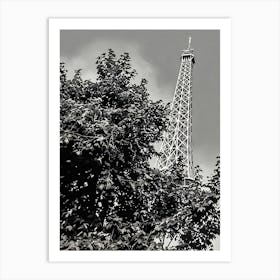 Eiffel Tower Behind Foliage. The image depicts the iconic Eiffel Tower partially obscured by dense foliage. The tower's intricate iron lattice structure rises prominently against a cloudy sky, creating a striking contrast with the dark leaves in the foreground. This juxtaposition of nature and architecture highlights the blend of urban and natural elements in Paris. Art Print