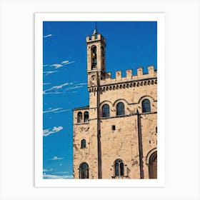 Palazzo dei Consoli (Palace of the Consuls) in Gubbio. A beautifully preserved medieval-style building with intricate stonework and arched windows under a vibrant blue sky. Its towering presence, complete with a clock tower, dominates a sunlit square where visitors stroll and admire the architecture. The scene captures the charm and history of a European town center. 2 Art Print