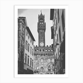 Palazzo Vecchio Florence. The image depicts a historic clock tower situated in a European city, framed by adjacent buildings. The tower features a prominent clock face and a crenellated top, with a flag flying at its peak. The surrounding architecture showcases a mix of stone and stucco facades, typical of old European urban design. Art Print