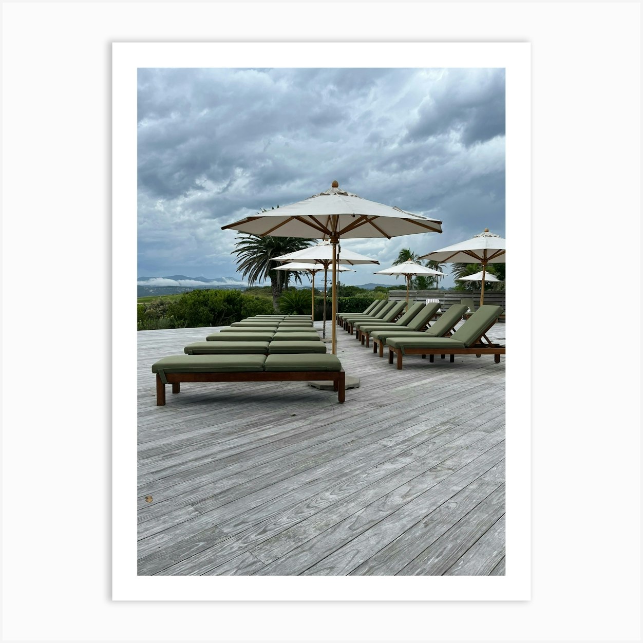 Outdoor Loungers and Umbrellas Against Overcast Landscape at Scenic Resort Art Print by I.Eye.Designs