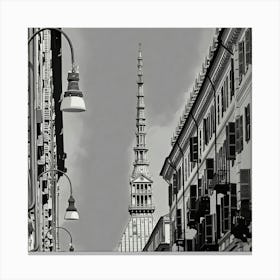 Urban View of a Historic Spire. The image depicts a black-and-white urban scene featuring a tall, ornate spire rising prominently in the center. The spire is framed by two rows of buildings with numerous windows and balconies, creating a symmetrical perspective. Street lamps hang from curved poles on the left side of the image, adding to the urban atmosphere. The architectural details and the height of the spire make it a focal point, suggesting it is a significant landmark. Canvas Print