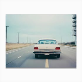 A Beige Vintage Car Drives Down A Street, With A Modern Apartment Building In The Background Canvas Print