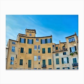 Piazza dell'Anfiteatro in Lucca. The vibrant Piazza dell'Anfiteatro in Lucca, Italy, is a unique elliptical square built on the remains of an ancient Roman amphitheater. Surrounded by colorful historic buildings, the square is bustling with life, featuring outdoor cafes, shops, and visitors enjoying the lively atmosphere. Canvas Print