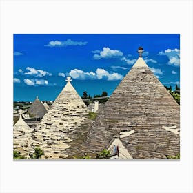 Trulli Houses in Italy. The image showcases a picturesque view of a traditional Italian village, featuring a cluster of Trulli houses with their distinctive conical roofs. The houses are constructed from white stone and have a rustic charm, with some roofs adorned with intricate patterns. The scene is bathed in warm sunlight, with a clear blue sky and fluffy white clouds overhead. 1 Canvas Print