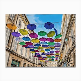 Colorful Umbrellas Street Art. A vibrant street scene features a multitude of colorful umbrellas suspended overhead, creating a whimsical and cheerful atmosphere. The umbrellas, in various shades of blue, green, purple, yellow, and pink, are strung across a narrow street lined with beige buildings. The buildings have white shutters and windows, adding to the European charm of the scene. Canvas Print