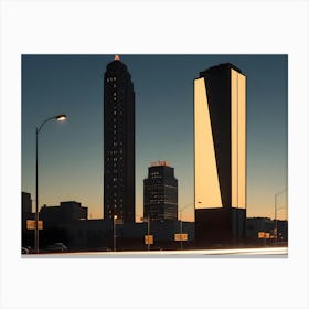 A Night Image Of City Buildings Illuminated With Lights Against A Dark Sky With Car Headlights Creating Streaks Of Light Canvas Print