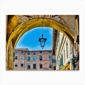 Lucca Under the Archway: A Glimpse of Historic Charm. This image captures a scenic view through a yellow-toned archway in a historic European city. A hanging lantern takes center stage, framed by rustic brick buildings and a bright blue sky, evoking the timeless allure of old-world architecture. Canvas Print