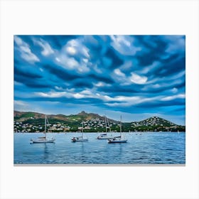 Sailboats at Anchor in Esterel France. The image captures a serene scene of several sailboats anchored in a calm bay. The boats are white with their masts raised, suggesting a peaceful and tranquil atmosphere. The water is a deep blue, reflecting the overcast sky above. The background features a picturesque coastline with rolling hills covered in lush greenery and dotted with houses. Canvas Print