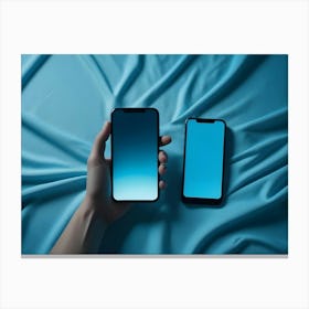 Two Smartphones Lie On A Blue Fabric With A Hand Holding One Canvas Print