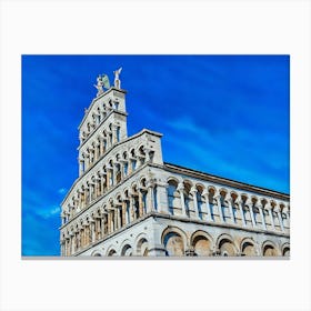 Lucca Majestic Facade: The Elegance of Romanesque Architecture. This image highlights the intricate facade of a Romanesque-style church under a vibrant blue sky. The series of arches, columns, and detailed sculptures create a harmonious display of historical craftsmanship, crowned by statues of angels that enhance the monument's grandeur. Canvas Print