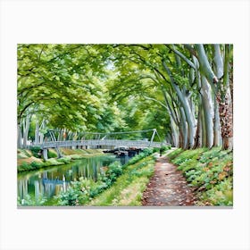 Tranquil Pathway near Canal de Brienne in Toulouse France. This image depicts a serene riverside scene with a narrow dirt path running alongside a calm river. The path is bordered by lush greenery and vibrant flowers, leading to a modern pedestrian bridge that spans the river. Tall trees with dense foliage arch over the path and river, creating a canopy of green. The reflection of the trees and bridge in the water adds to the tranquil atmosphere. Canvas Print