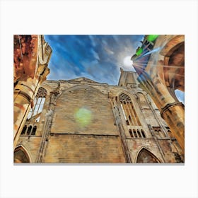 Stone Archway and Tower in Narbonne. The image captures a low-angle view of a weathered stone building with a prominent archway and a tower. The sun shines brightly in the blue sky, casting a warm glow on the aged stonework. The archway leads to a shadowy interior, while the tower stands tall against the clouds. 1 Canvas Print