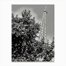 Eiffel Tower Behind Foliage. The image depicts the iconic Eiffel Tower partially obscured by dense foliage. The tower's intricate iron lattice structure rises prominently against a cloudy sky, creating a striking contrast with the dark leaves in the foreground. This juxtaposition of nature and architecture highlights the blend of urban and natural elements in Paris. Canvas Print