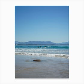 Surfers On The Beach In Popular, Byron Bay. Town And Mountains In The Background, In The Distance Over The Ocean Canvas Print