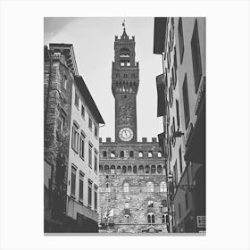 Palazzo Vecchio Florence. The image depicts a historic clock tower situated in a European city, framed by adjacent buildings. The tower features a prominent clock face and a crenellated top, with a flag flying at its peak. The surrounding architecture showcases a mix of stone and stucco facades, typical of old European urban design. Canvas Print