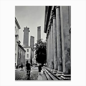 Towers and Columns in Pavia Italy. A black and white photograph captures a narrow street lined with tall, slender towers, their tops reaching towards a cloudy sky. The towers are made of stone and have a weathered, aged appearance. On the right side of the image, a row of imposing columns stands tall, creating a sense of grandeur and history. Canvas Print