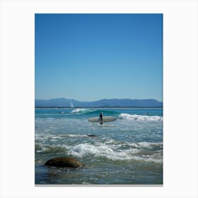 Surfer On The Beach With Surfboard Amongst Blue Skies, Rocks And Mountain Background In Byron Bay, Queensland Canvas Print